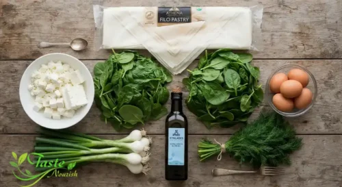 Flat lay of raw ingredients filo sheets, fresh spinach, block of feta, eggs, spring onions, dill, olive oil