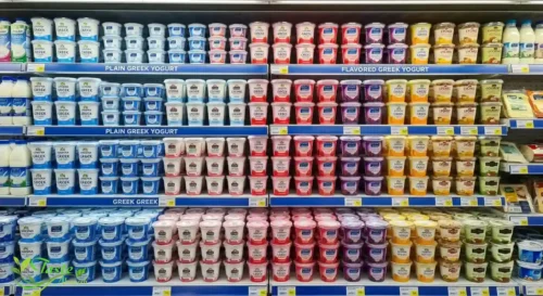 Grocery store dairy aisle shelf stocked with plain and flavored Greek yogurt