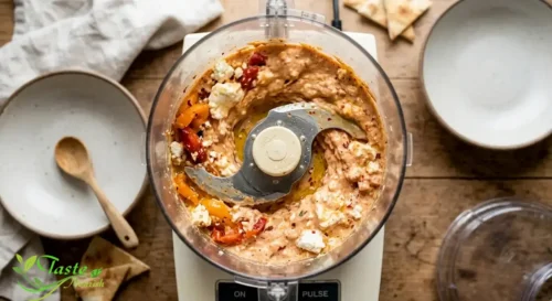 Food processor blending roasted red peppers with feta and cream cheese
