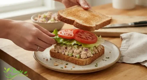 Tuna salad sandwich being assembled with lettuce and tomato